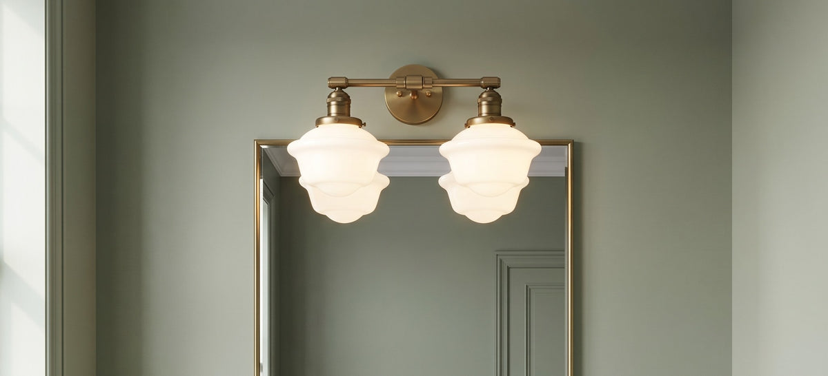 Ely two light vanity light in antique brass above a brass framed mirror in a sage green panelled bathroom