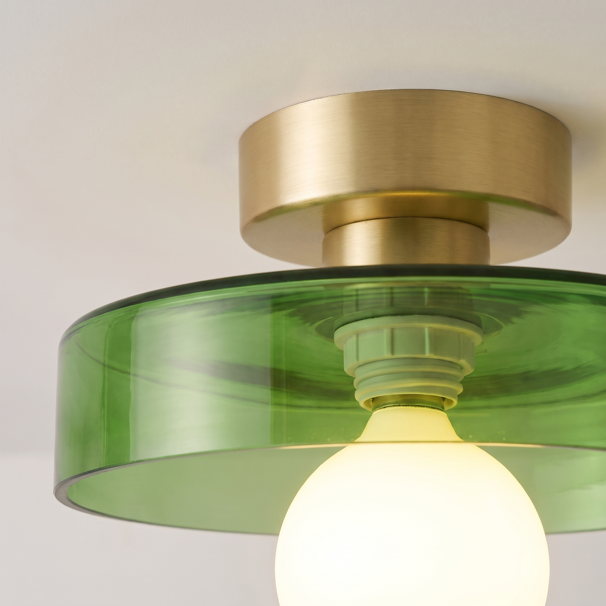 Close up of the Bawdsey green glass disc, brass canopy and globe bulb, lit