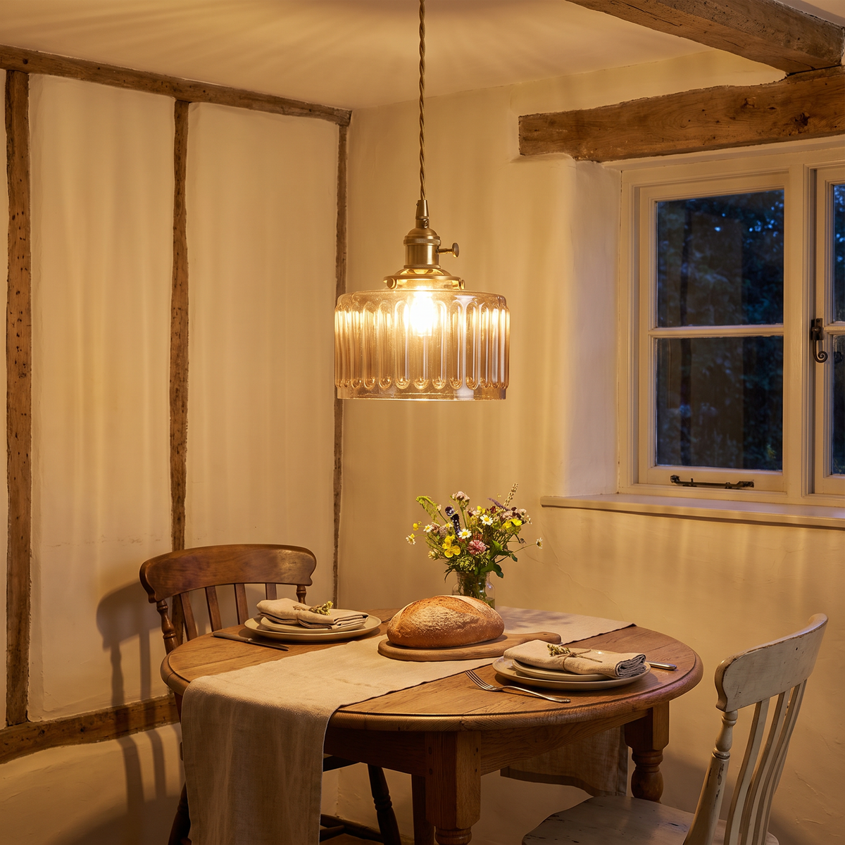 Amber Bildeston ribbed glass pendant lit over a round oak dining table in a cottage dining room