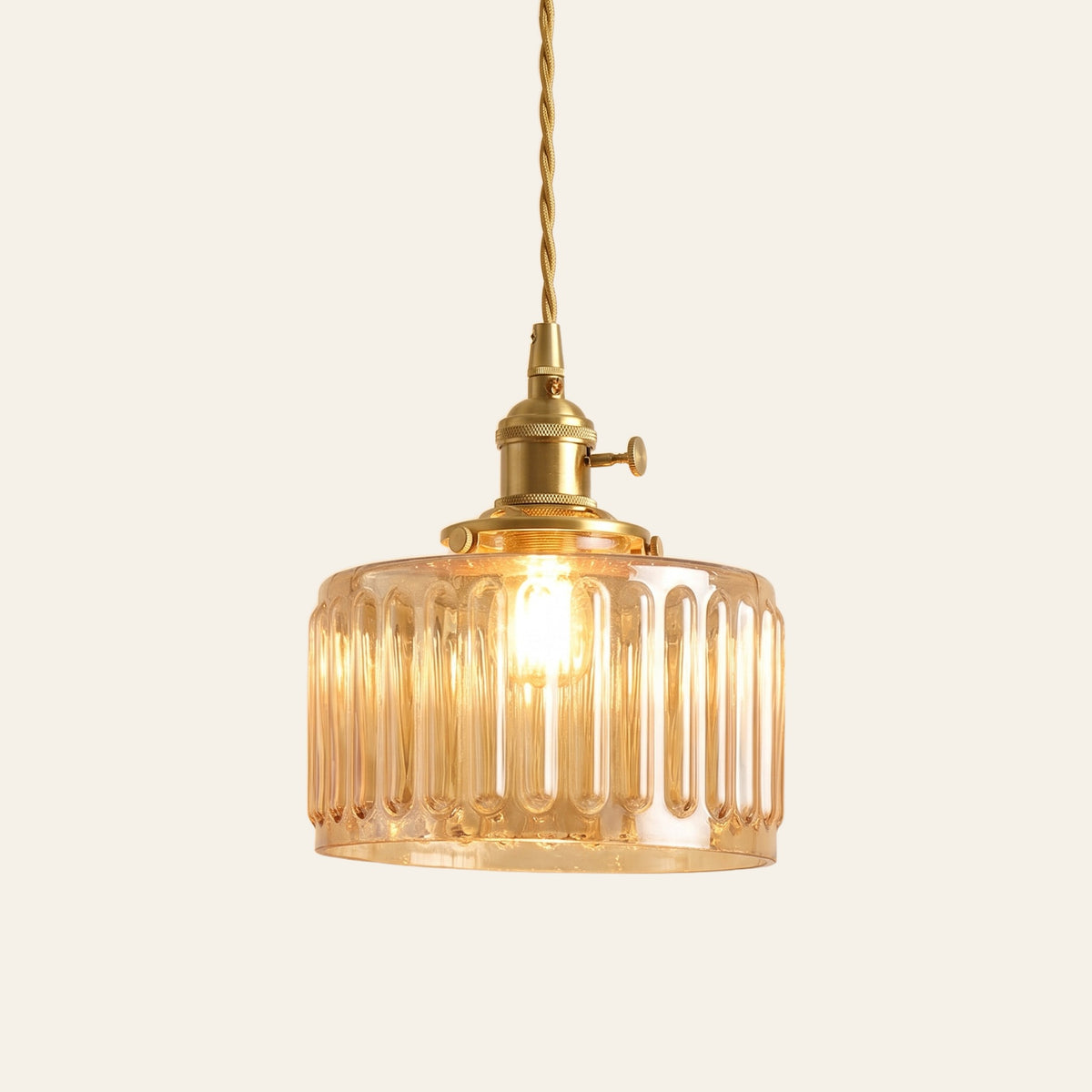 Bildeston ribbed glass drum pendant light in amber glass on a brass holder with a twisted cord, cream background