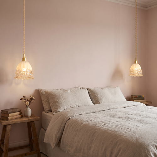 A pair of lit Bramfield glass bell pendants either side of a bed
