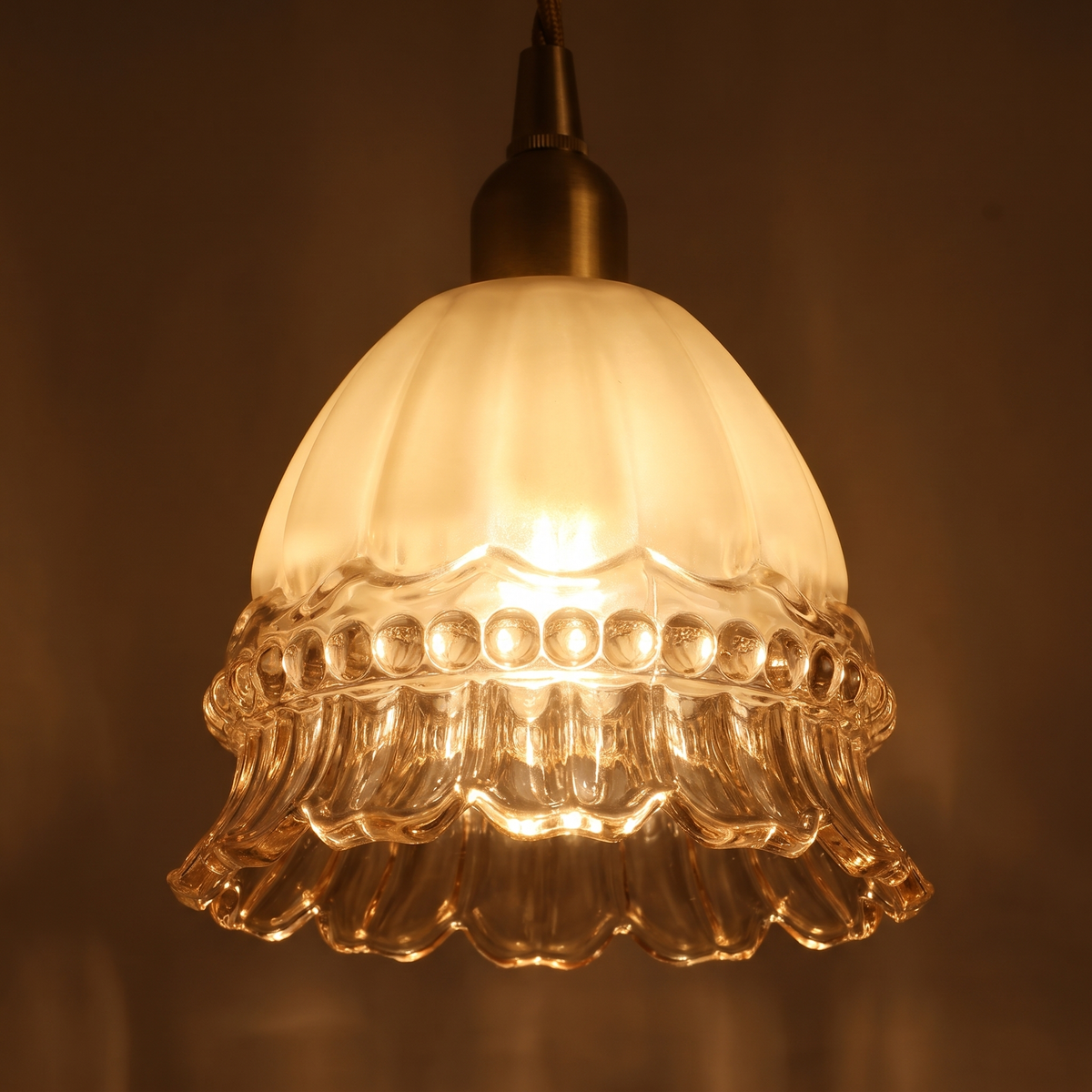 Close up of a lit Bramfield shade showing the milky fluted glass, beaded band and clear ruffled rim