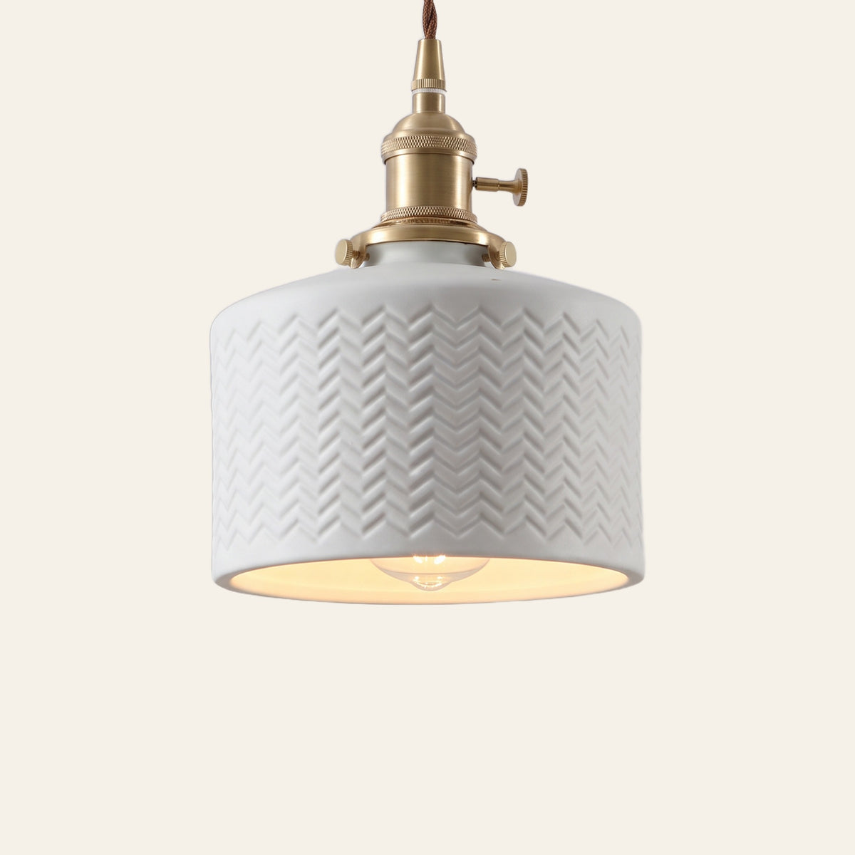 Brantham pendant light, a matte white ceramic drum with a pressed chevron pattern on a brass finish holder, lit, cream background