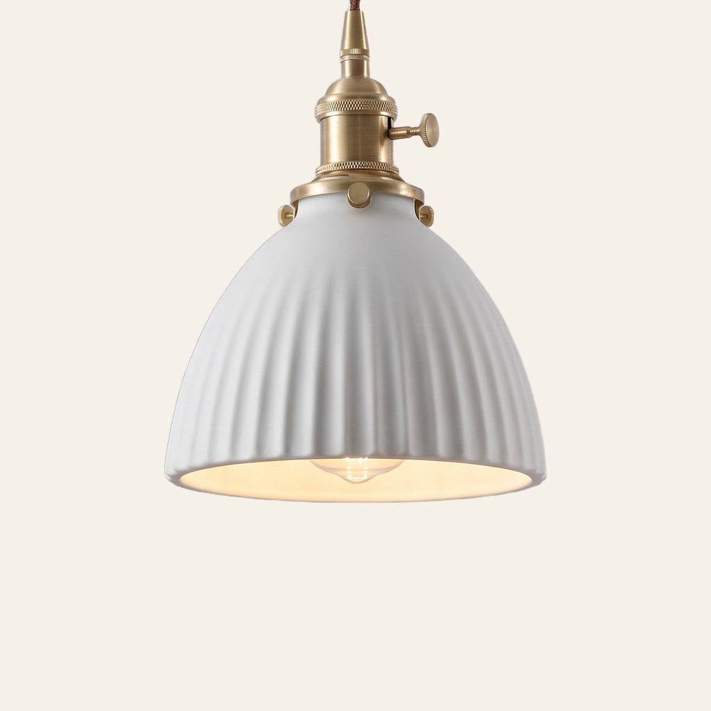 Brantham pendant light, a matte white ribbed ceramic bell shade on a brass finish holder with a turn switch, lit, cream background