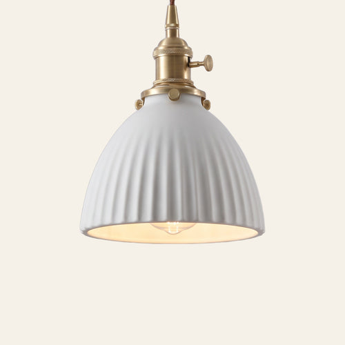 Brantham pendant light, a matte white ribbed ceramic bell shade on a brass finish holder with a turn switch, lit, cream background
