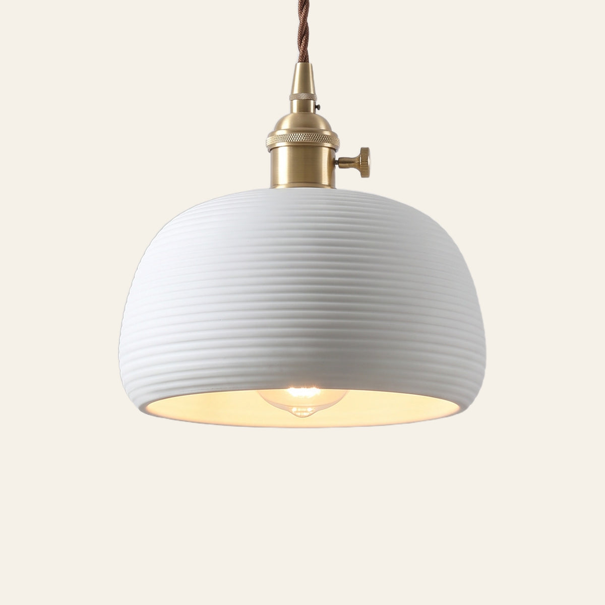 Brantham pendant light, a rounded matte white ceramic shade with fine rings on a brass finish holder, lit, cream background