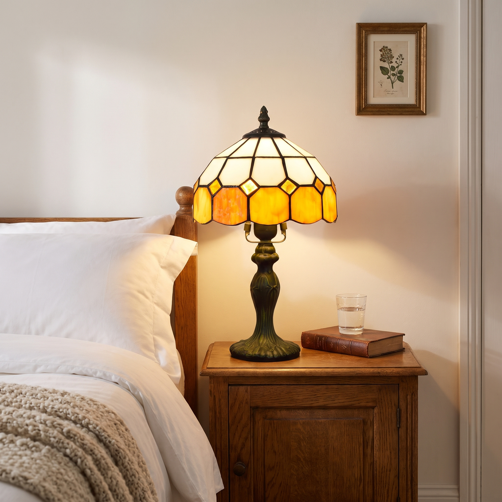 Amber Cavendish stained glass lamp lit on a wooden bedside cabinet beside a white bed