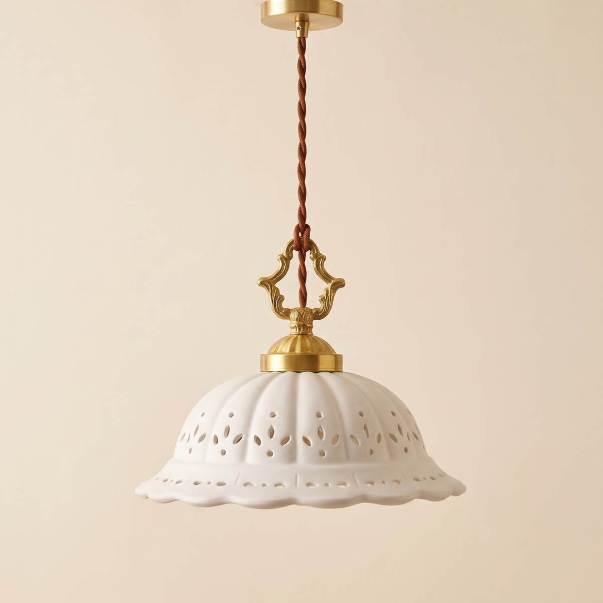 Dennington pendant light with a white pierced ceramic dome, ornate brass finish loop and braided cord, cream background