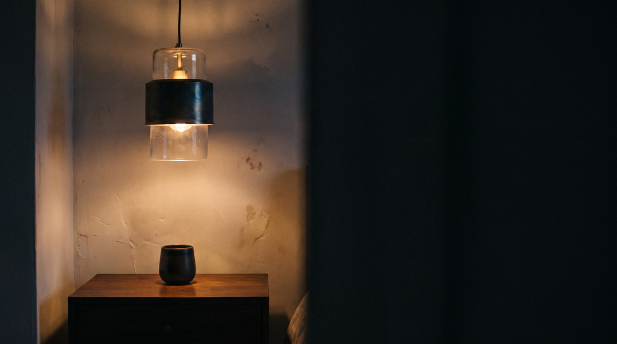 Lit bronze pendant light casting a warm pool of light in a dark room at night