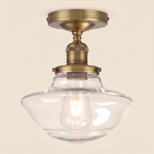 Ely clear glass semi flush ceiling light in antique brass with a clear schoolhouse shade and filament bulb, lit, cream background