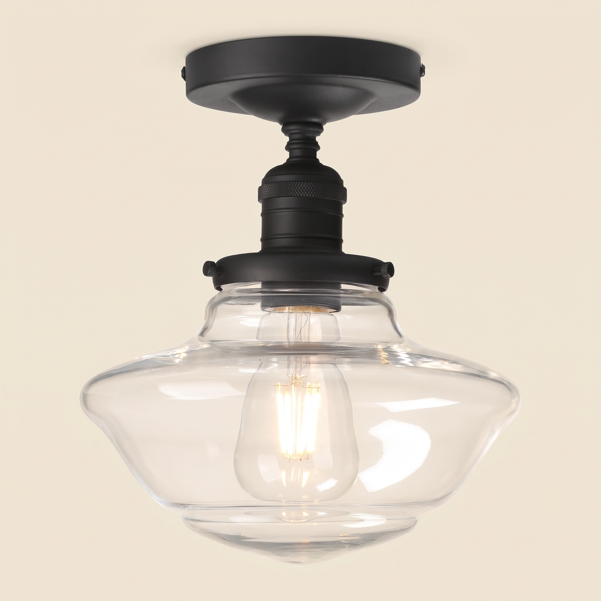 Ely clear glass semi flush ceiling light in black with a clear schoolhouse shade and filament bulb, lit, cream background
