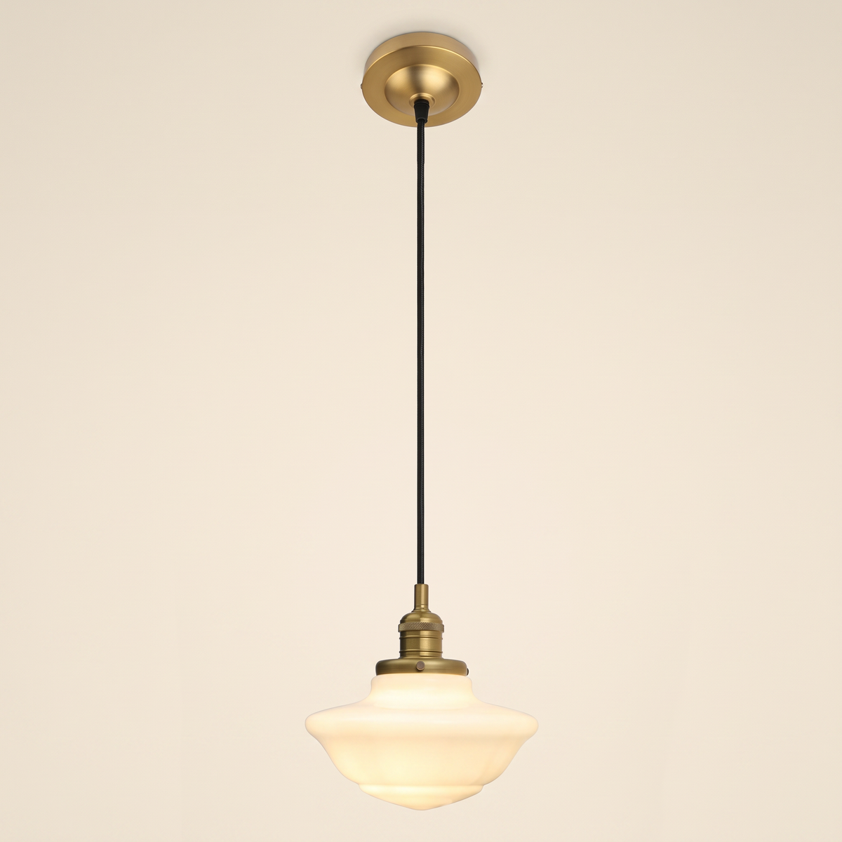 Ely pendant light with a stepped opal milk glass schoolhouse shade on a black cord, antique brass lamp holder and ceiling plate, cream background