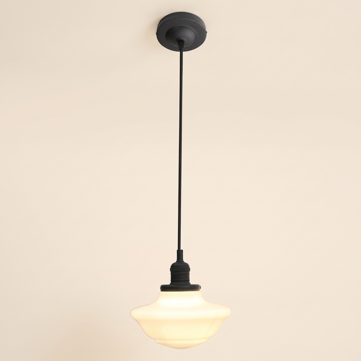 Ely pendant light with a stepped opal milk glass schoolhouse shade on a black cord, black lamp holder and ceiling plate, cream background