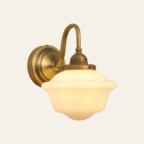 Ely swan neck wall light in antique brass with a stepped opal milk glass schoolhouse shade, lit, cream background