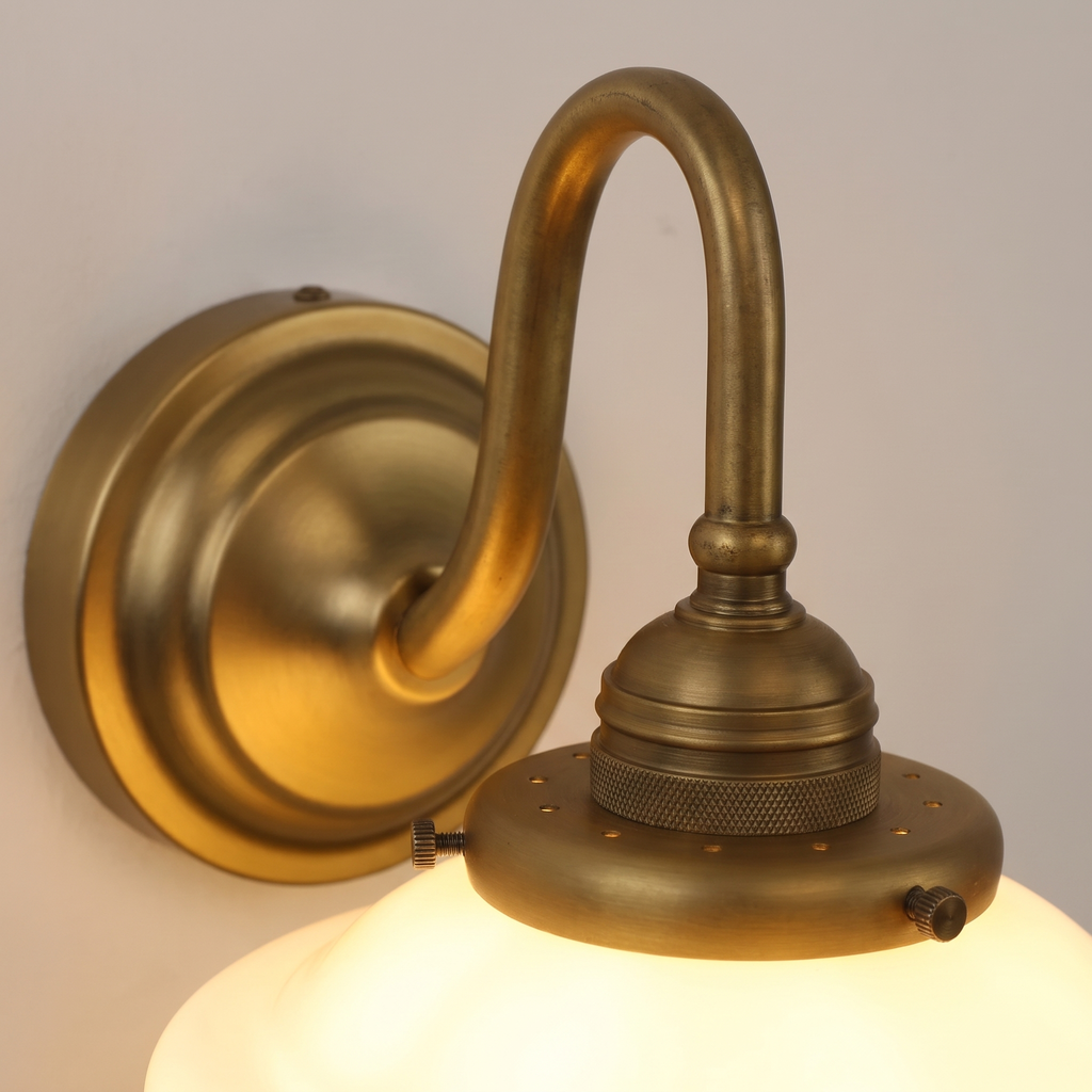Close up of the antique brass swan neck arm and gallery on the Ely wall light above the opal glass shade
