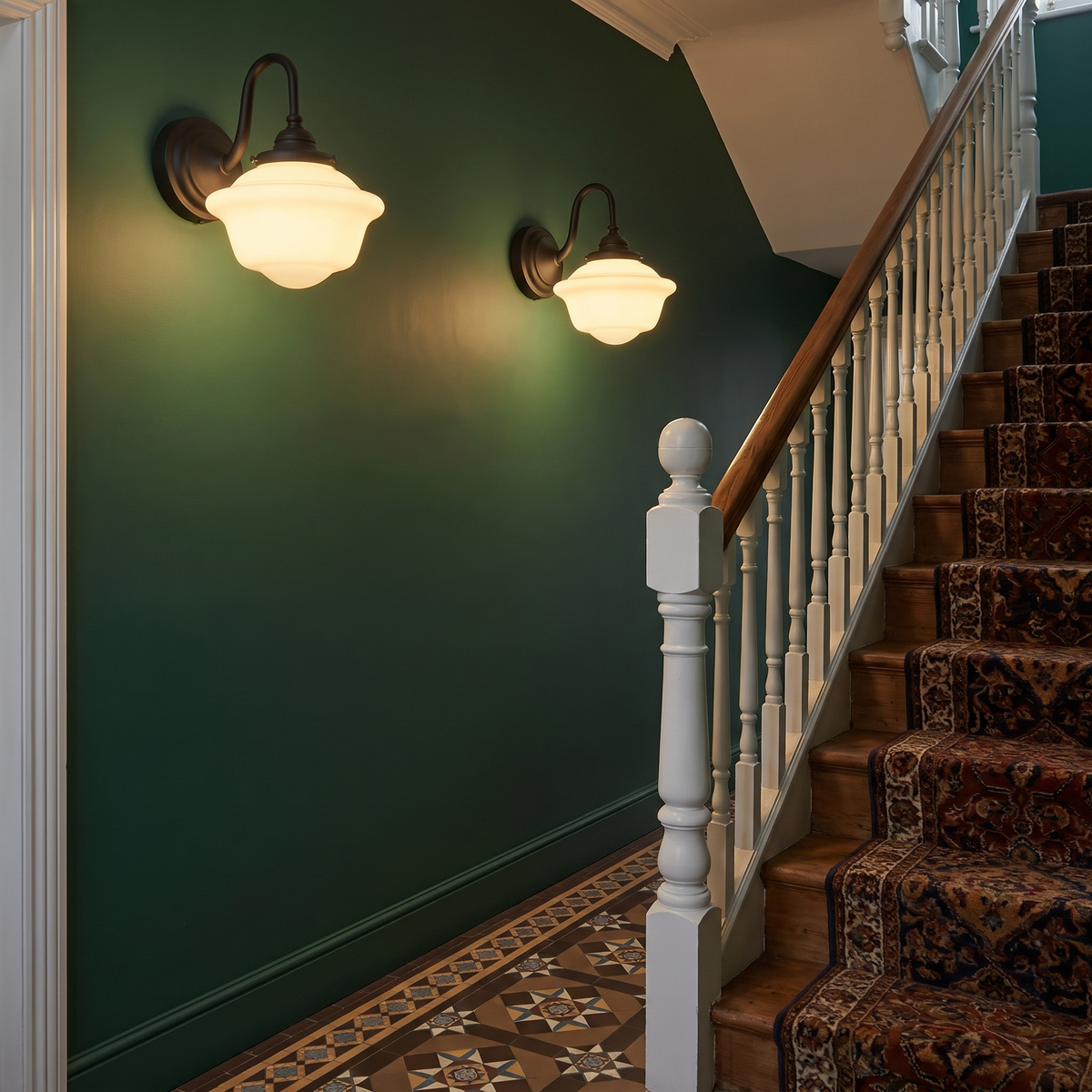 Two lit black Ely swan neck wall lights on a deep green hallway wall beside the stairs