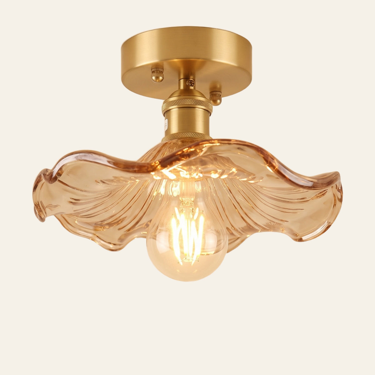 Framlingham ceiling light with a wavy amber glass lotus leaf shade on a brass stem, lit