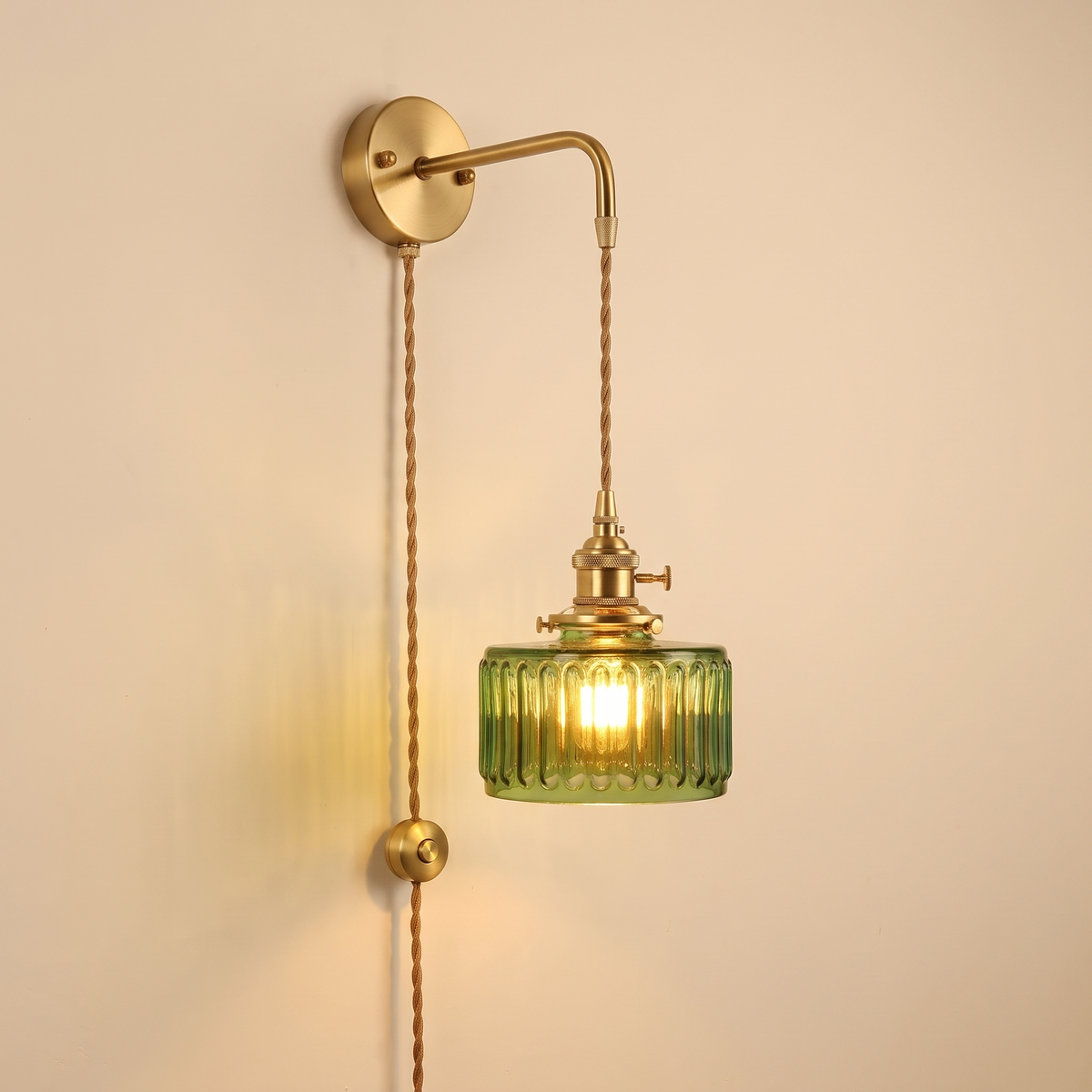 Framsden wall light with a green ribbed glass shade, plug in version with a braided cable and a button switch running down the wall, lit, cream background