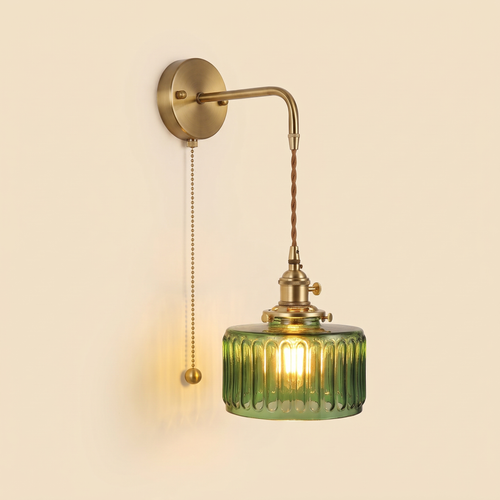 Framsden wall light with a green ribbed glass drum shade hanging on a braided cord from a brass coloured bracket, with a pull chain, lit, cream background