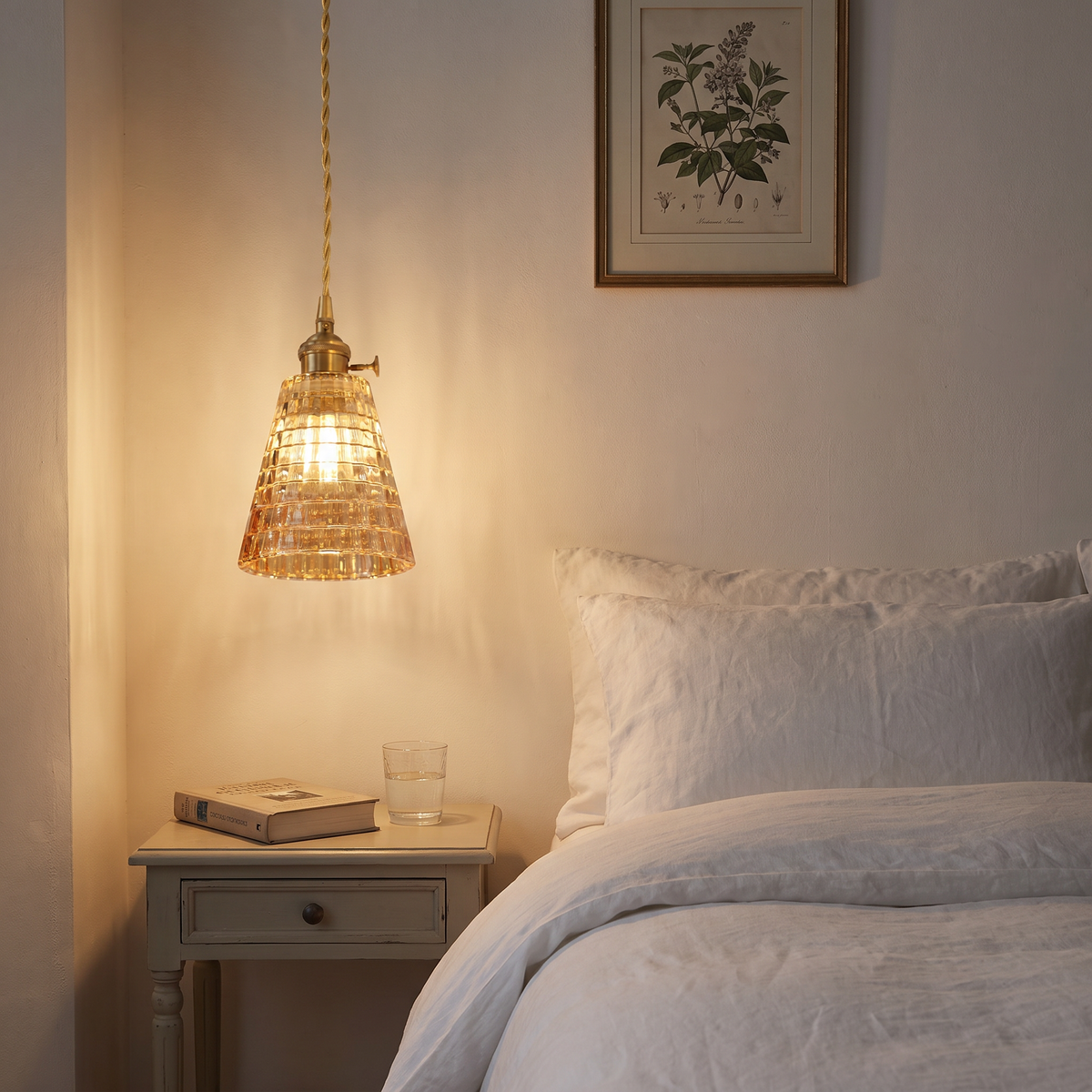 A Hacheston amber cut glass pendant lit low beside a bed