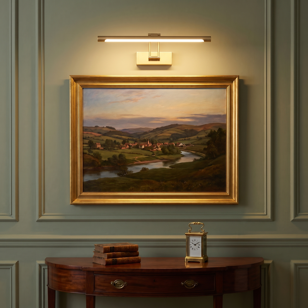 A lit brushed gold Helmingham picture light above a gilt framed landscape painting on a sage green panelled wall