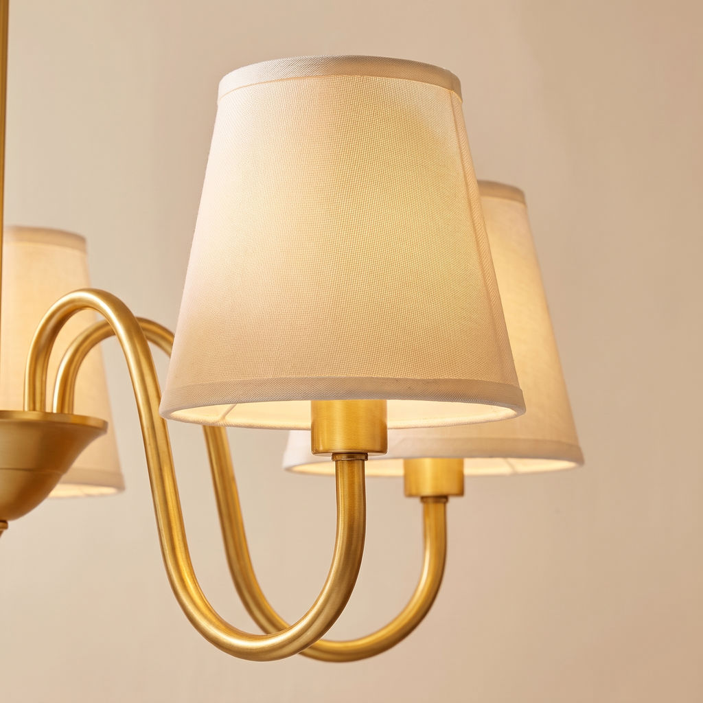 Close up of the Henham cream linen shades on curved brass coloured arms, lit