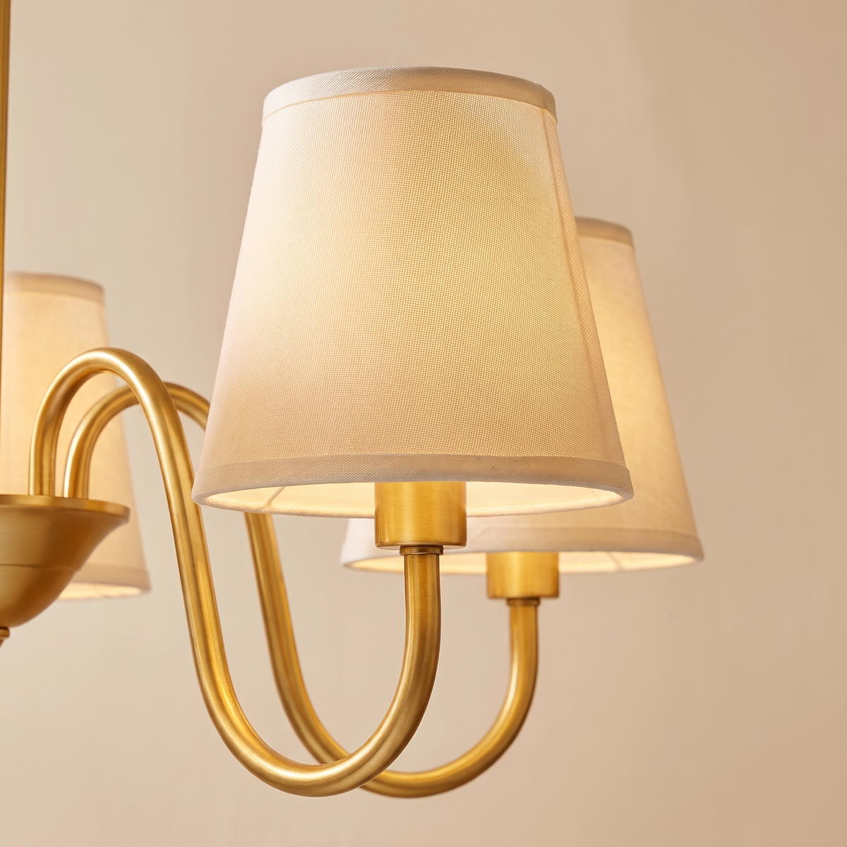 Close up of the Henham cream linen shades on curved brass coloured arms, lit