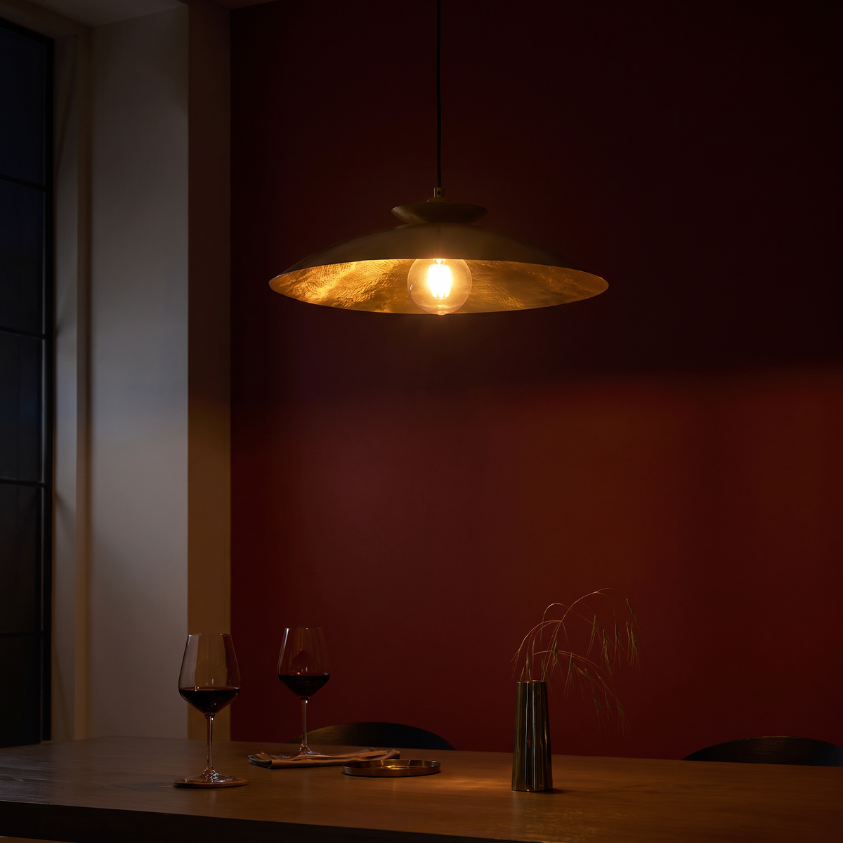 Halvern brass disc pendant lit above a dining table in the evening