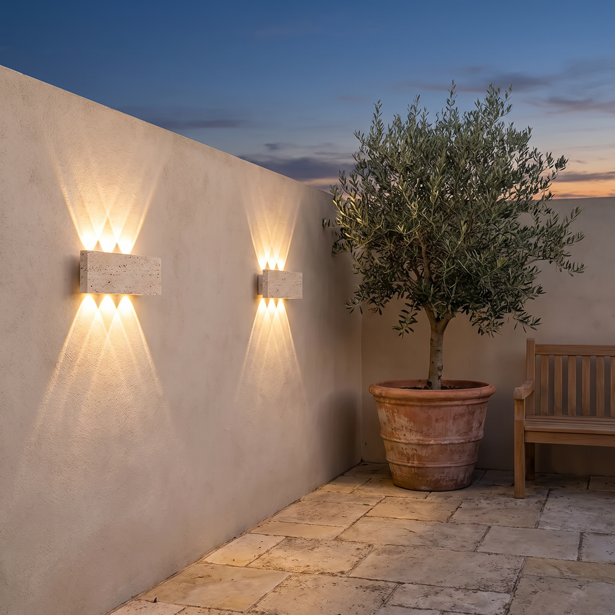 Two Purbeck lights along a garden wall beside an olive tree at dusk