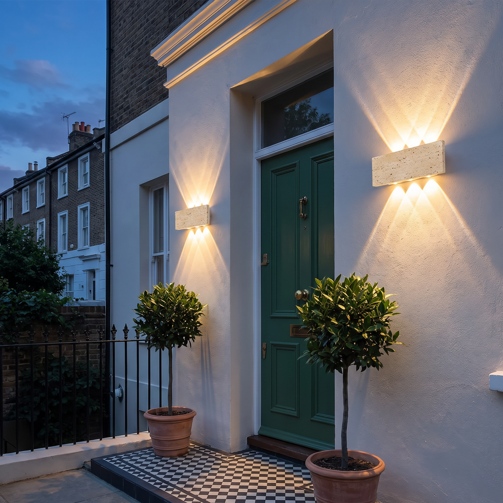 A pair of Purbeck stone wall lights either side of a green front door at dusk