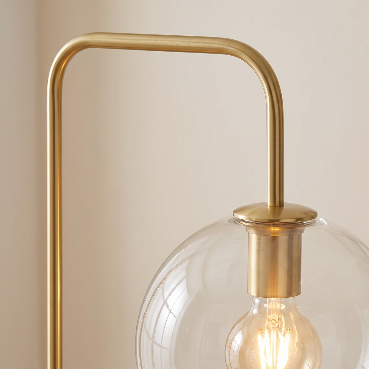 Close up of the Clifton gold arm, lamp holder and clear glass globe with a filament bulb