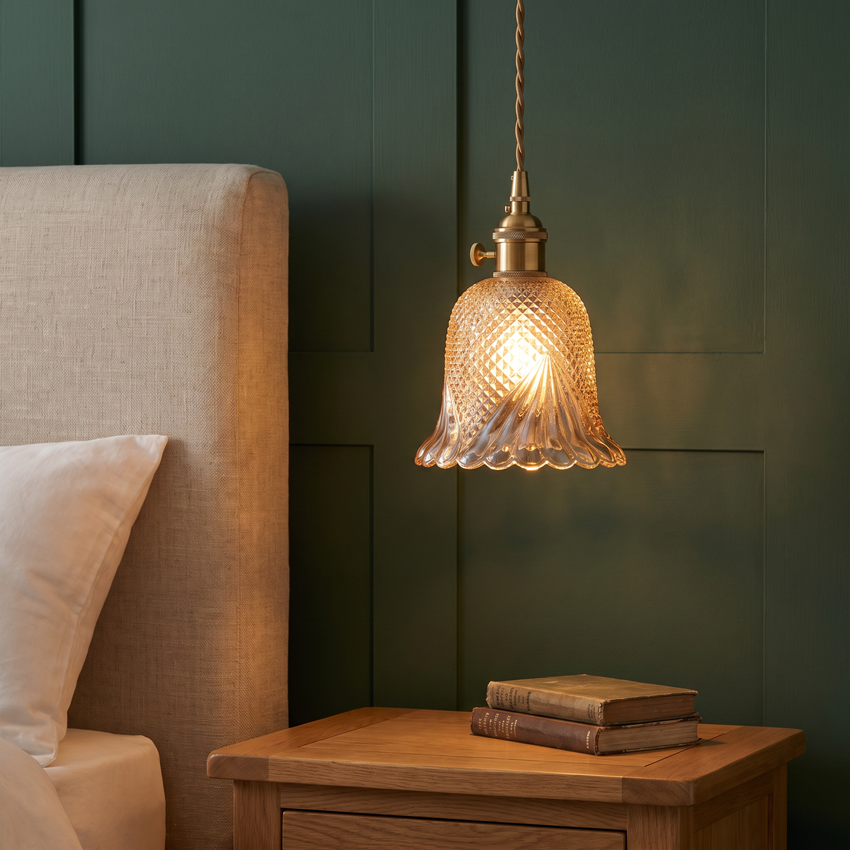 Amber Lavenham cut glass pendant light glowing beside a bed against dark green panelling