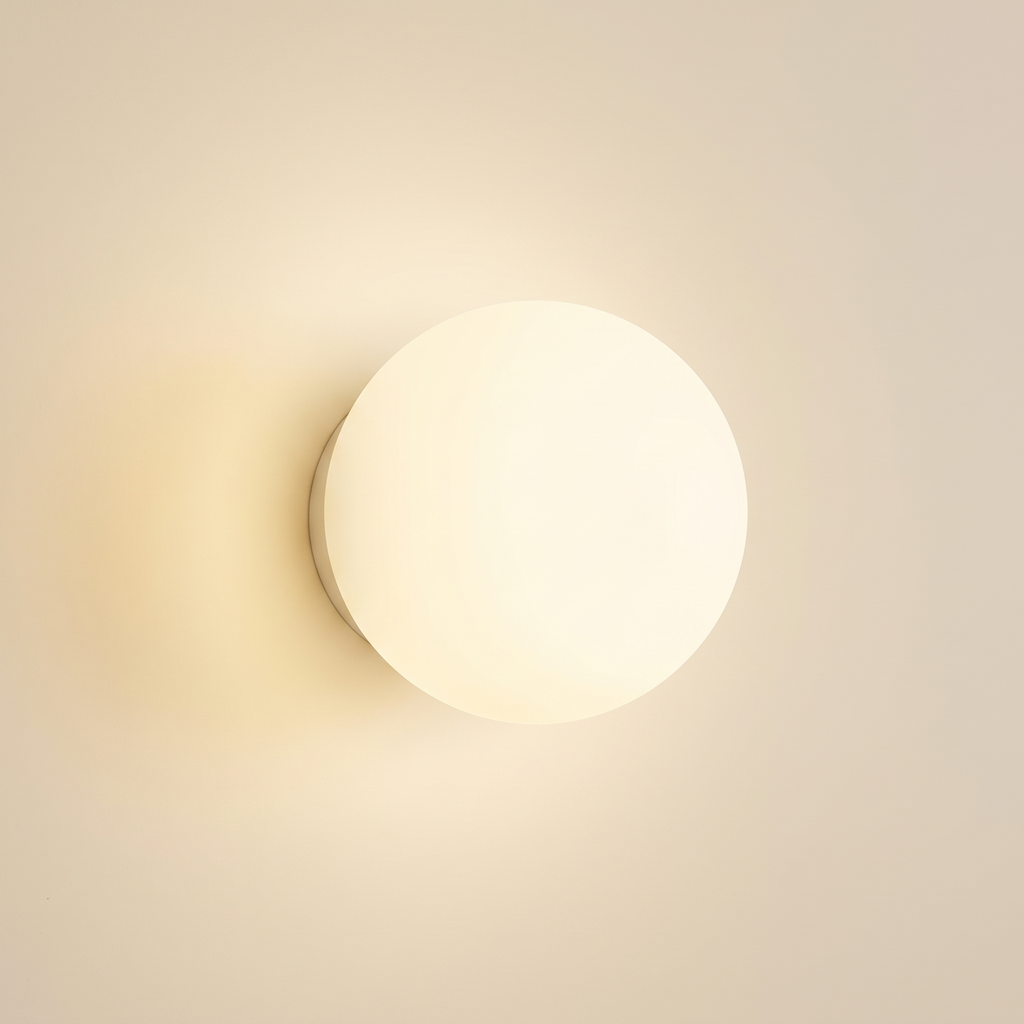 Aldeburgh frosted opal glass globe wall light, lit on a cream wall