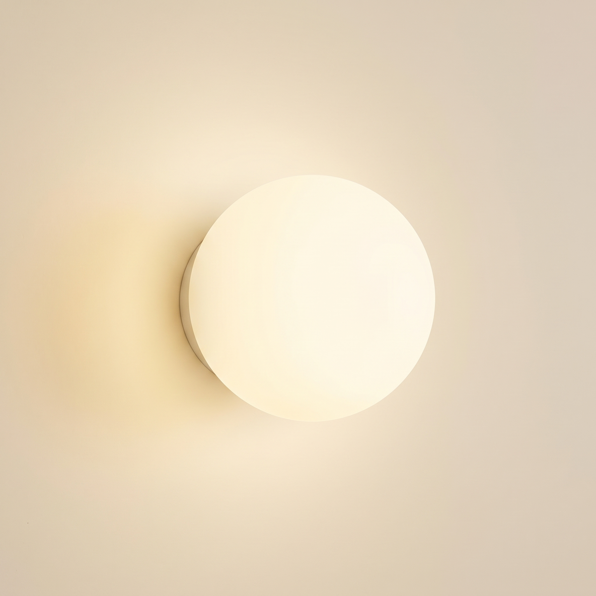 Aldeburgh frosted opal glass globe wall light, lit on a cream wall