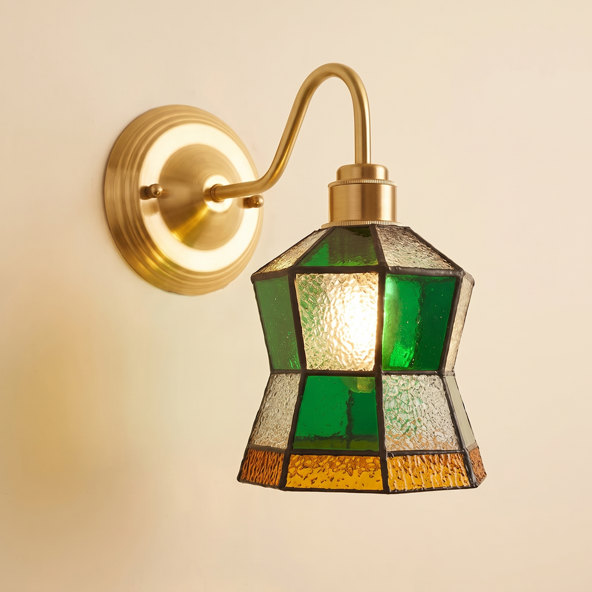 Walberswick stained glass wall light with a green, clear and amber lantern shade on a brass swan neck arm, lit