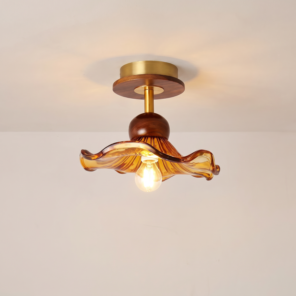 Blakeney semi flush ceiling light with an amber ruffled glass shade, walnut toned wood and brass, lit