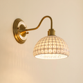 Wangford wall light with a white ceramic basket weave dome on a brass swan neck arm, lit