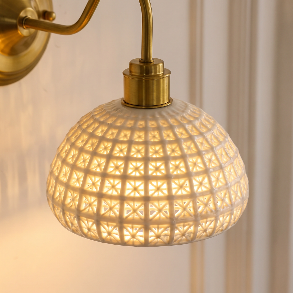 Close up of the Wangford white ceramic basket weave dome glowing, with its brass holder