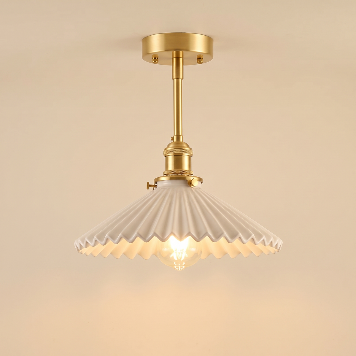 Debenham semi flush ceiling light with a white pleated ceramic shade on a brass rod, lit