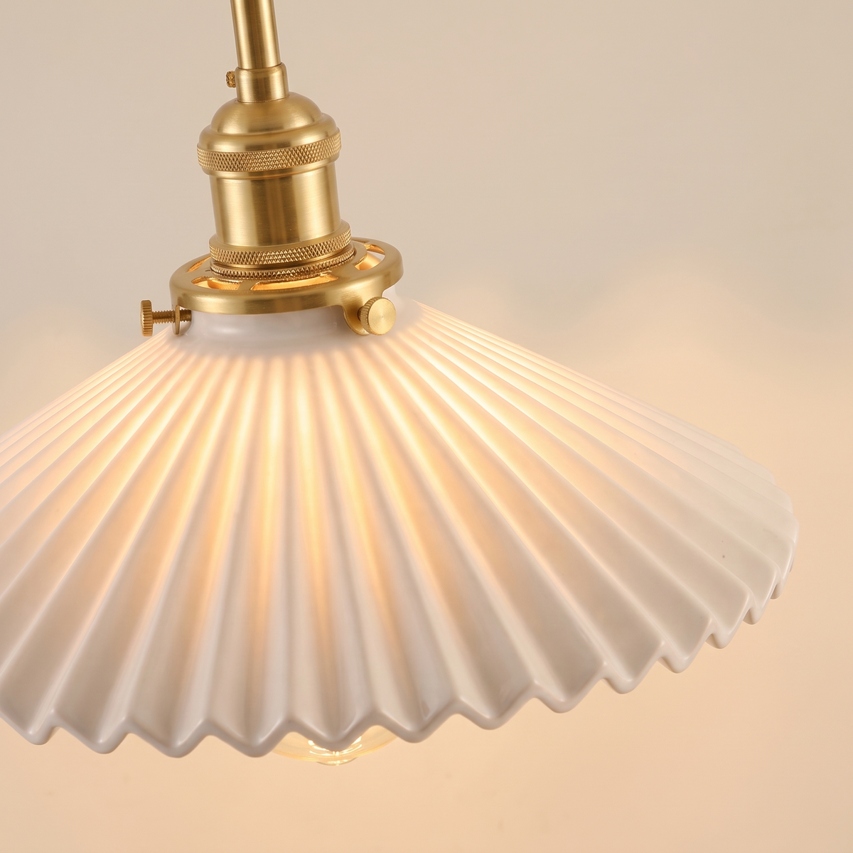 Close up of the Debenham white pleated ceramic shade glowing, with its brass holder