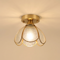 Hadleigh flush ceiling light with six petals of clear textured glass in a brass frame, lit