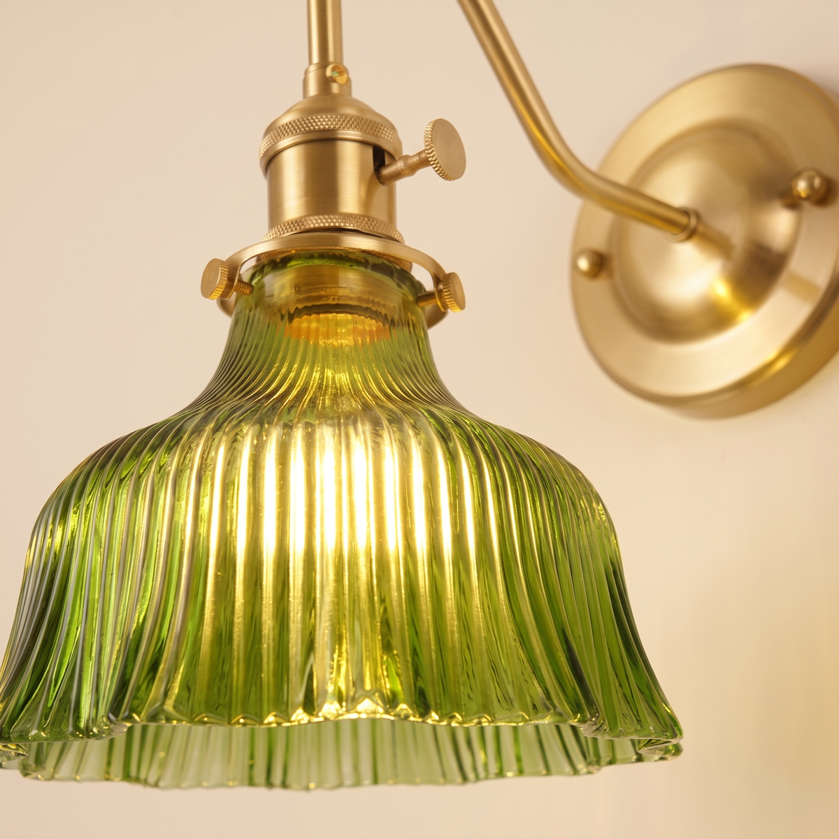 Close up of the Nayland fluted green glass bell shade and brass holder with its turn knob switch, lit
