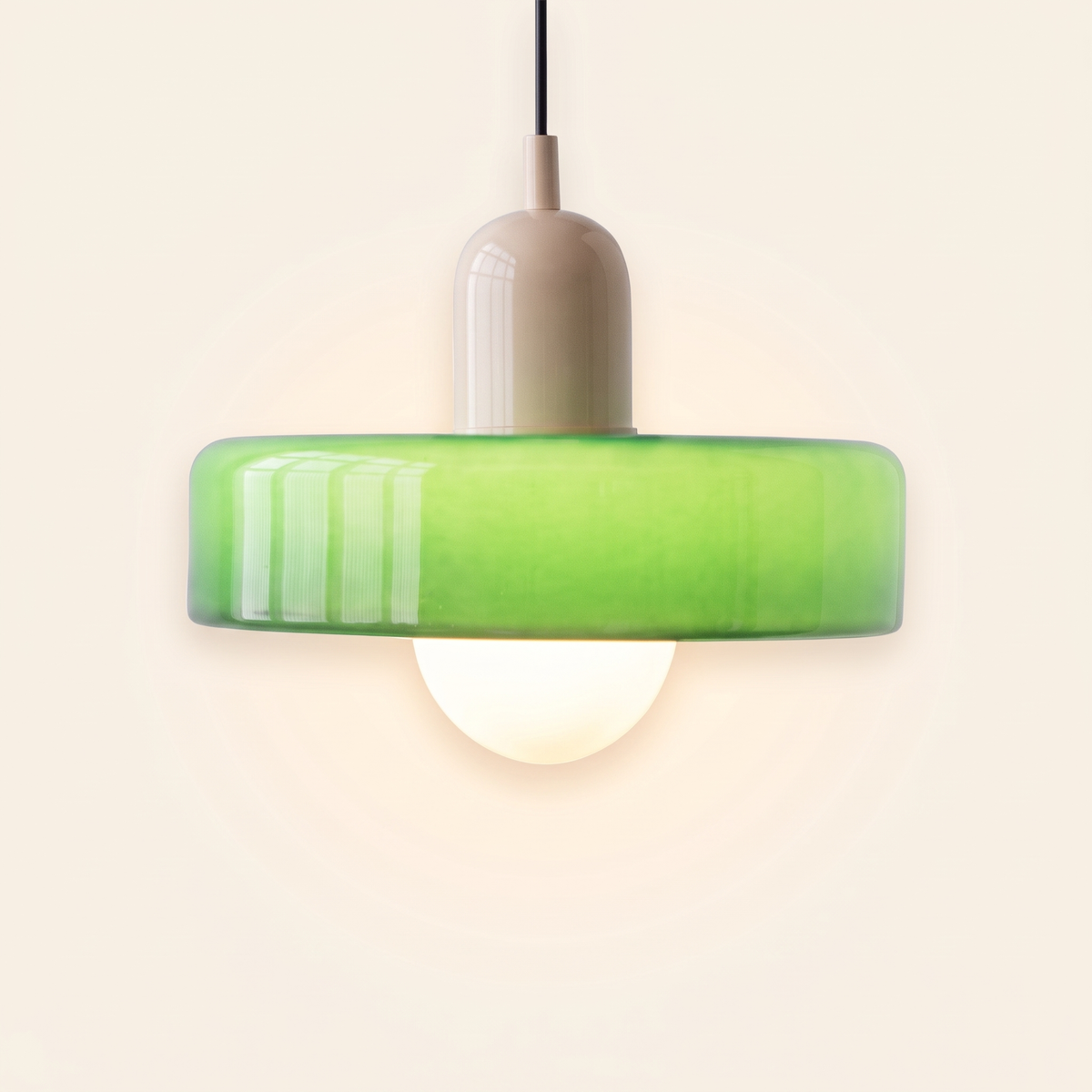 Welwyn mid century glass pendant light, green glass disc with a cream cap, lit, on a cream background