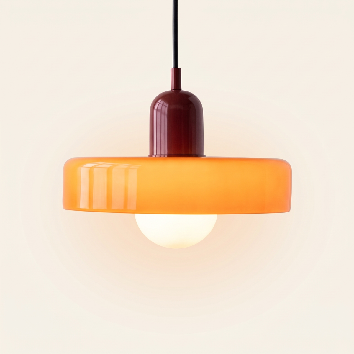 Welwyn mid century glass pendant light, orange glass disc with a burgundy cap, lit, on a cream background