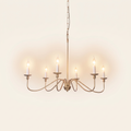 Ashworth gold six light candle chandelier, lit, on a cream background