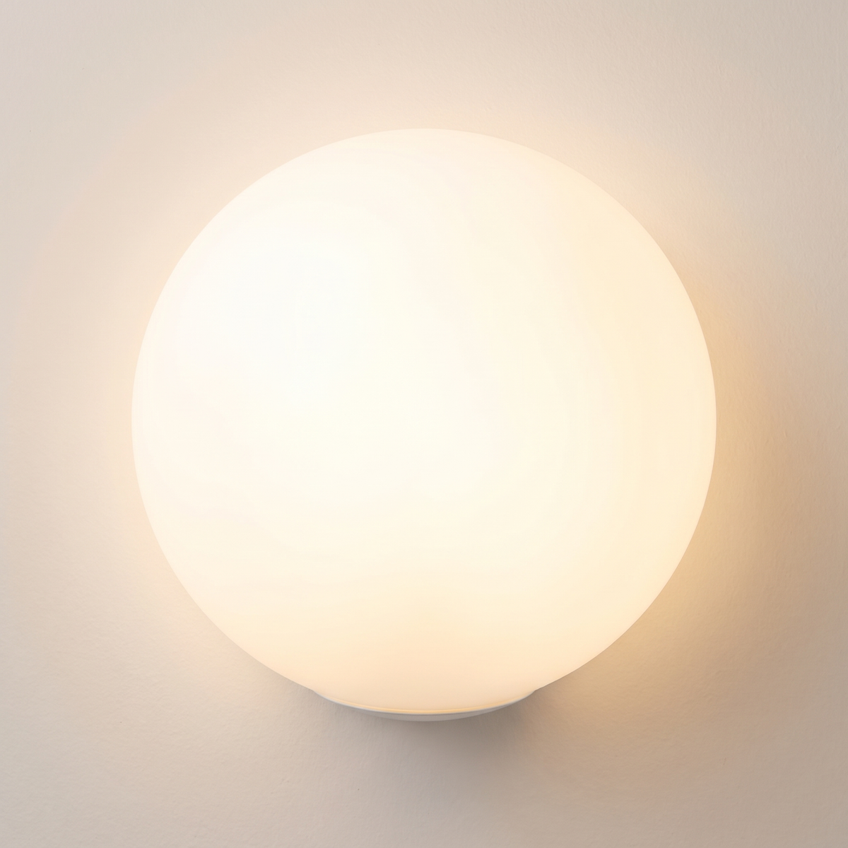 Selwyn 20 cm opal glass globe wall light, lit, glowing on a warm wall