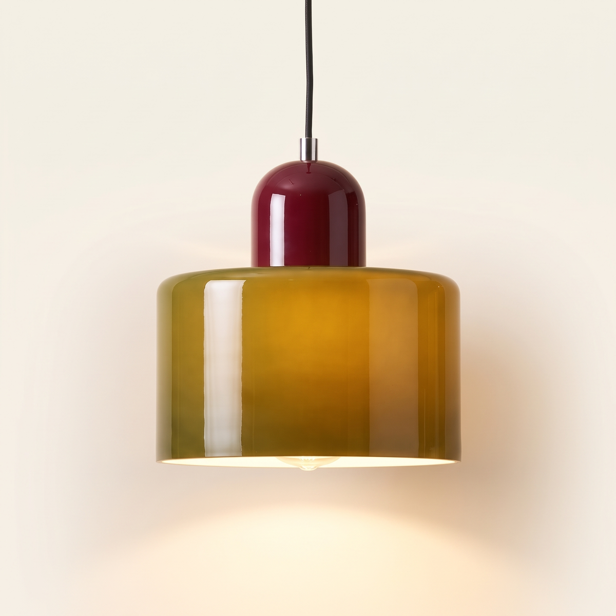 Thaxted mid century glass drum pendant light, olive glass with a wine red cap, lit, on a cream background