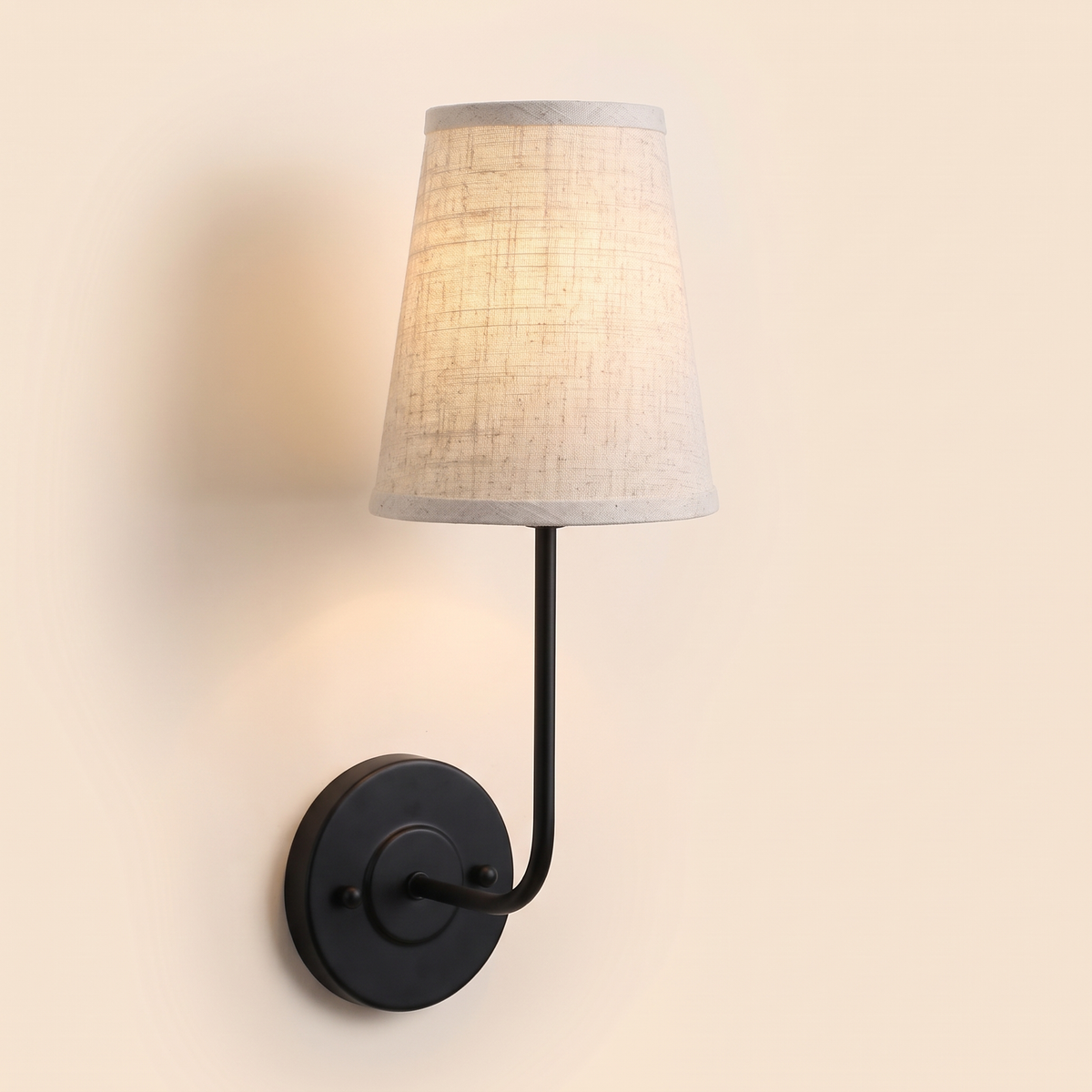 Hintlesham wall light in black with a natural linen shade, lit, cream background