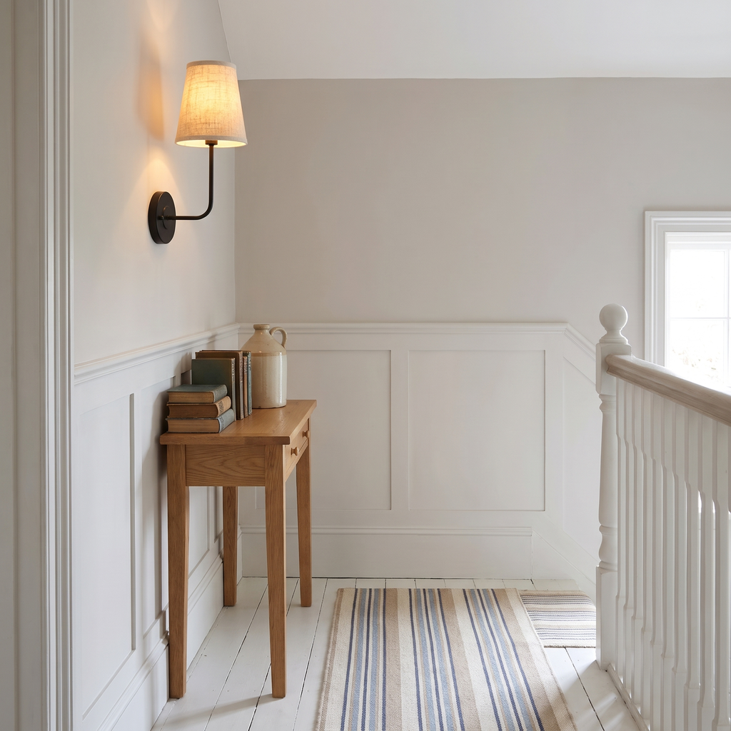 A lit black Hintlesham wall light above white panelling on a hallway landing