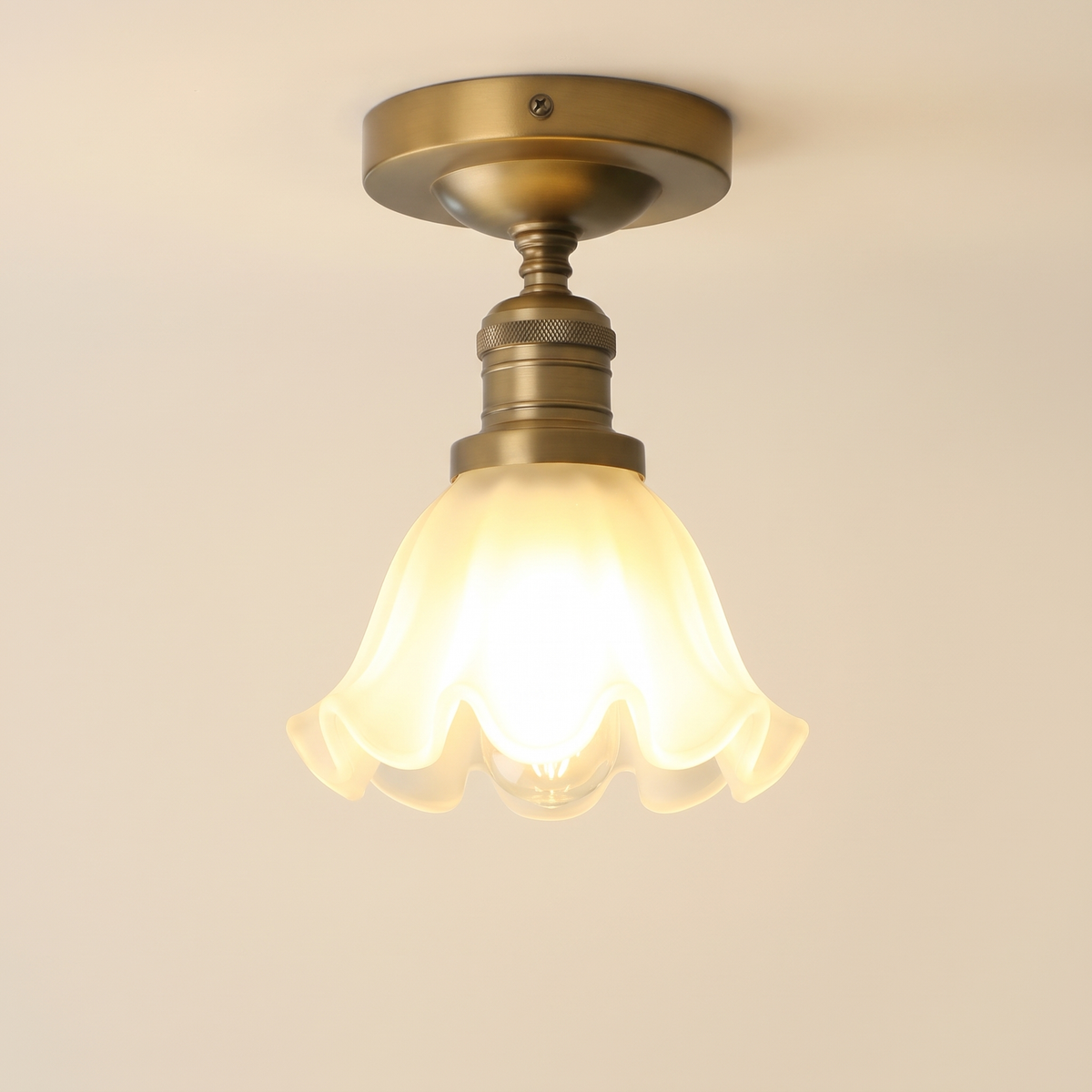 Hoxne semi flush ceiling light in antique brass with a frosted ruffled tulip glass shade, lit, cream background